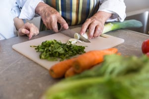 close-up-of-a-senior-lady-cutting-vegetables-on-a--PSRBJBT